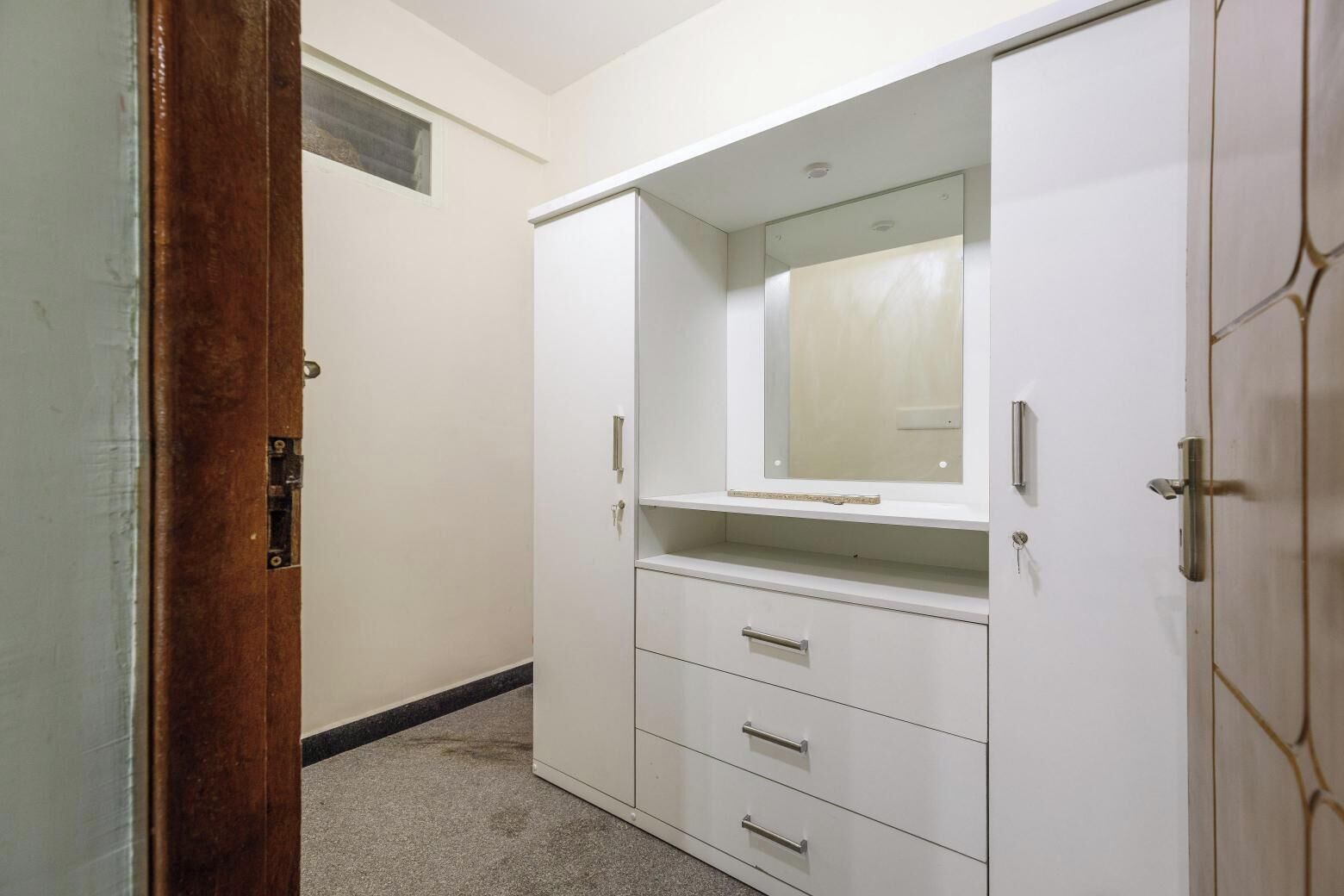 Ein weißer Kleiderschrank mit Spiegel und zwei Schubladen, eine Holztür und ein Teppichboden.