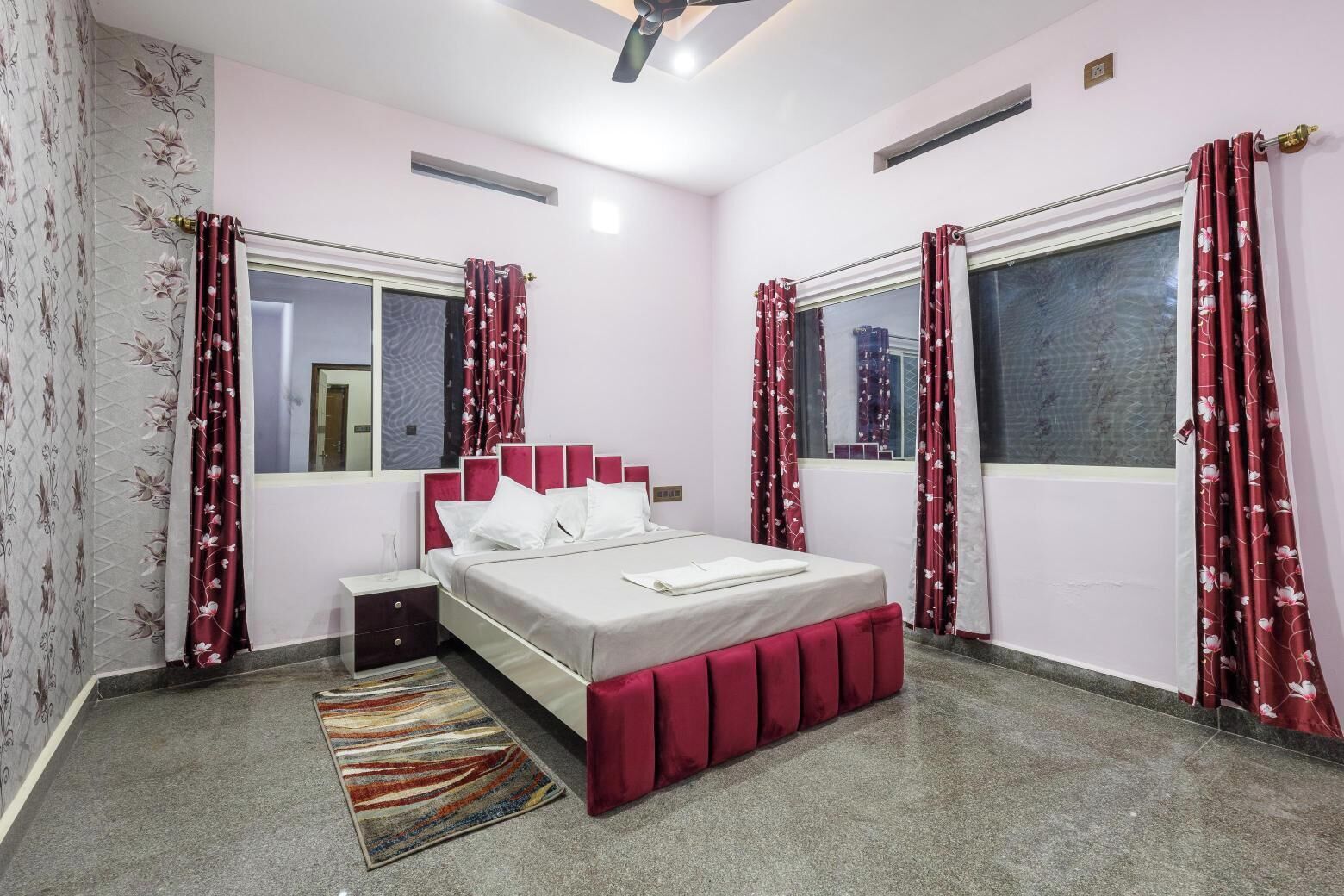 Un dormitorio con cama, mesitas de noche, alfombra y cortinas.