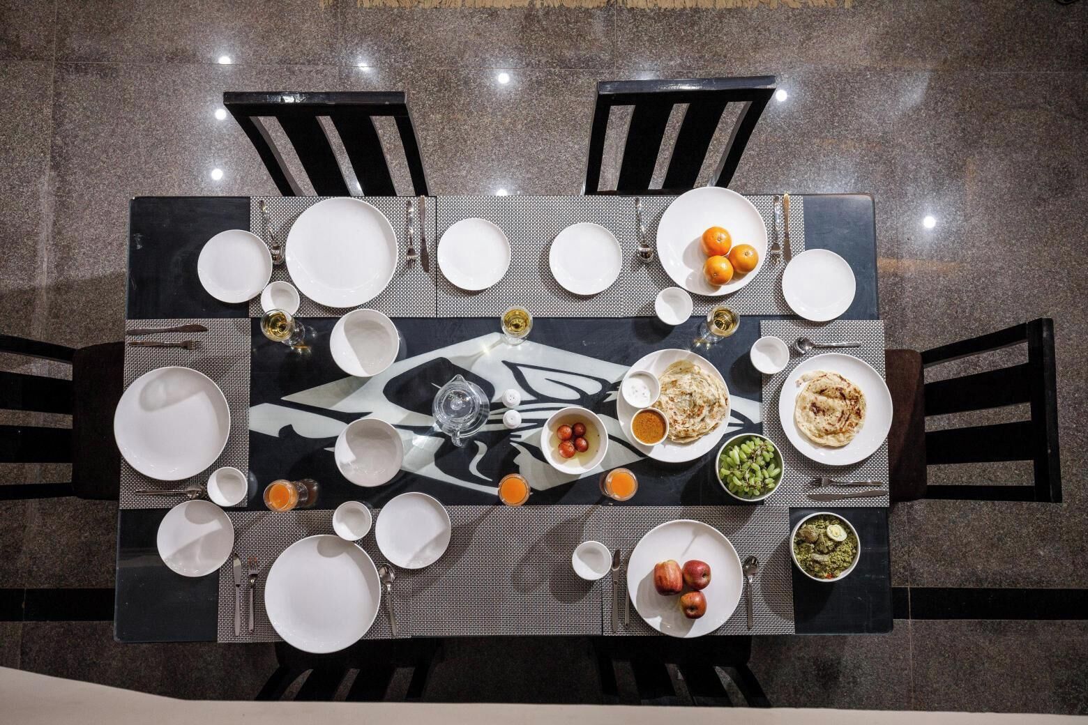 A dining table set with plates, bowls, and glasses, surrounded by chairs.