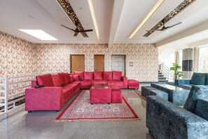 A spacious living room with a red sectional sofa, blue armchairs, a glass coffee table, and a patterned rug. - Forest Grove by Stayjade Poolbonfire 1hr E-city (Denkanikota)