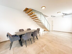 Ein modernes Interieur mit einem Esstisch und Stühlen, einer Treppe mit Holzstufen und einem Glasgeländer.