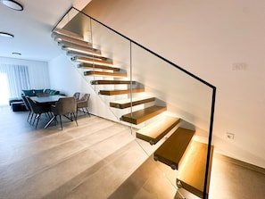 Eine moderne Treppe mit Glastrennläufen und Holzboden, die zu einem Essbereich mit Tisch und Stühlen führt.