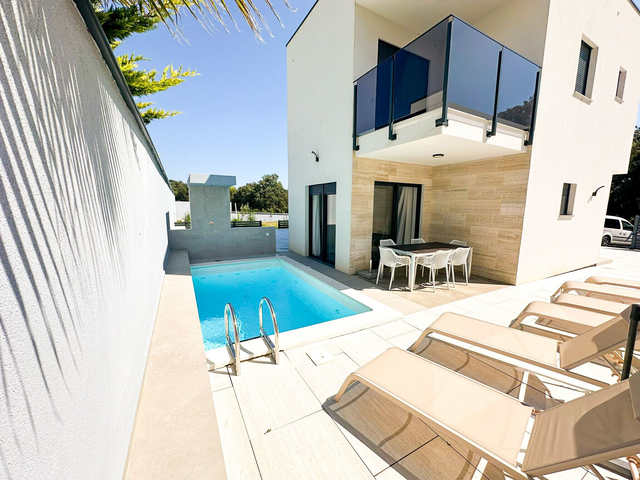 A modern outdoor pool area with a clear blue pool, a sun lounger, and a dining area with outdoor furniture.