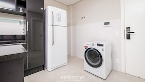 A compact kitchen with a refrigerator, washing machine, and a built-in oven. - Modern Studio 4 Minutes From Jurere Beach Elu207 (Florianópolis)