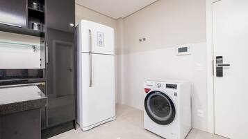 A compact kitchen with a refrigerator, washing machine, and a built-in oven.