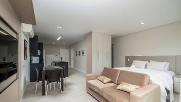 A modern hotel room with a bed, a sofa, a dining area, and a kitchenette.