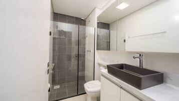 Un baño moderno con ducha de vidrio, inodoro blanco y un lavamanos rectangular grande con encimera de mármol.
