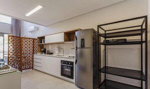 Una cocina moderna con horno integrado, refrigerador y una estantería metálica negra.