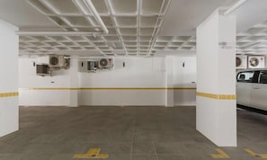 Un garaje para estacionar con paredes blancas, piso cubierto de baldosas amarillas y múltiples unidades de aire acondicionado montadas en las paredes.