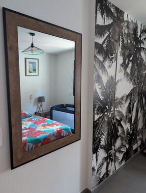 A bedroom with a bed, a bedside table, a lamp, and a wall-mounted mirror.