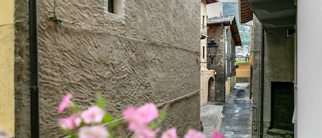 A narrow alleyway with stone buildings, a visible window, and a street lamp.