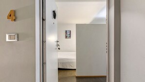 Une chambre d’hôtel avec un lit, une porte, un interrupteur fixé au mur et une affiche accrochée au mur.