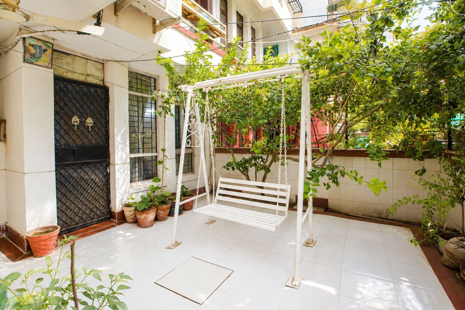 Une balançoire blanche avec un banc, entourée de plantes en pot et posée sur un sol carrelé.