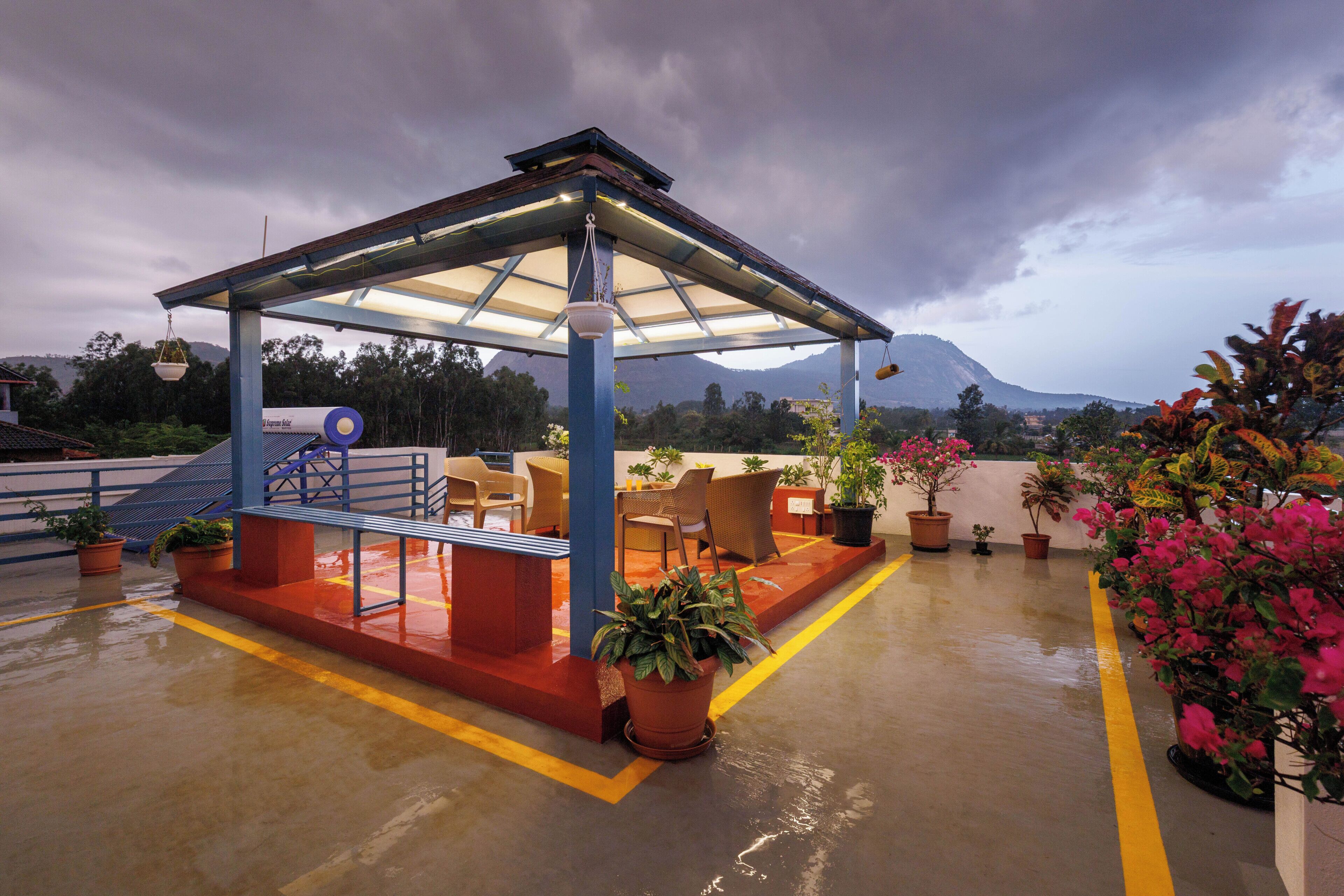 A covered outdoor seating area with chairs and tables, surrounded by potted plants and a view of a mountain.