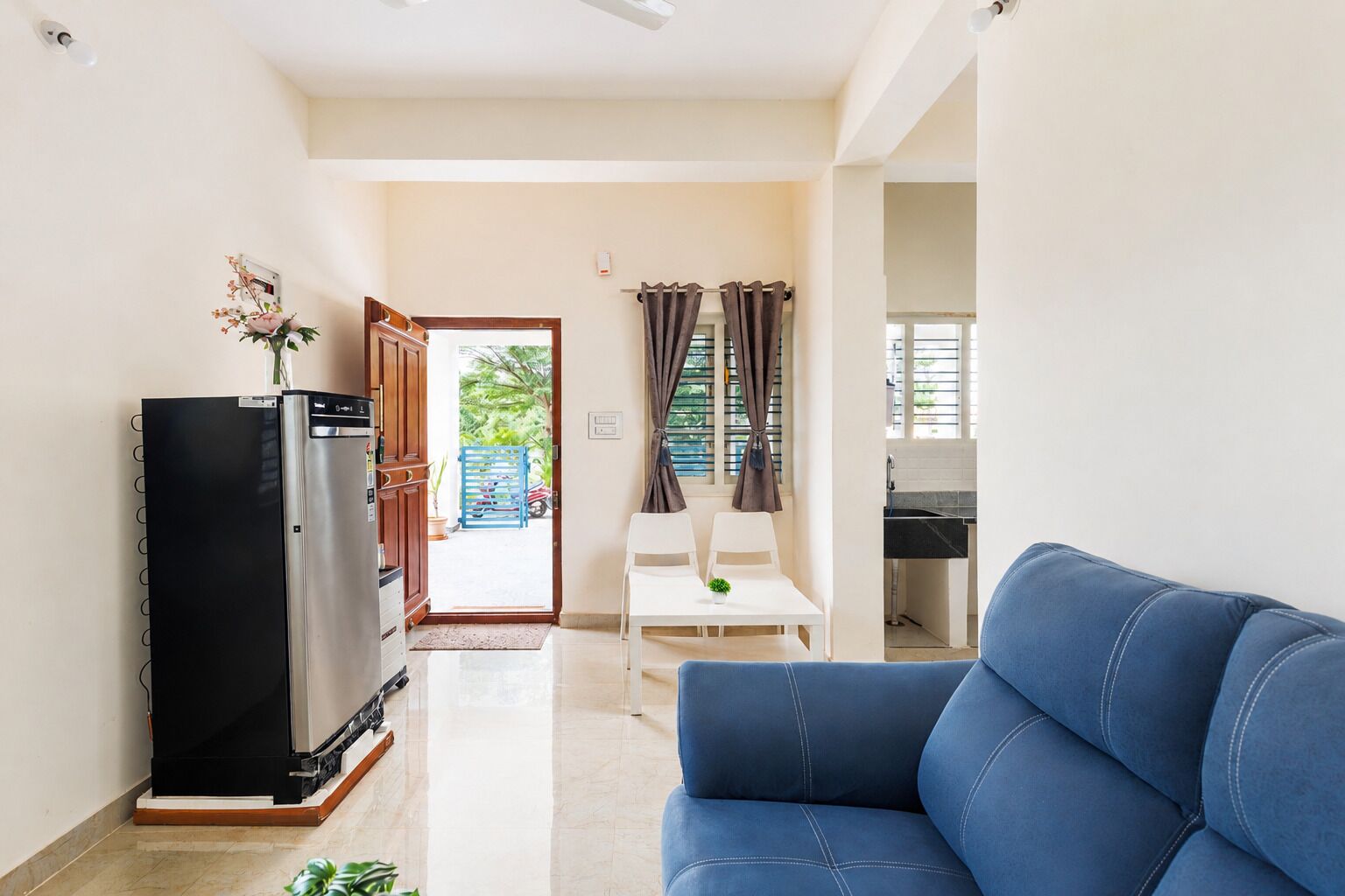 A living room with a sofa, a refrigerator, a dining table with chairs, and a view of the outside.