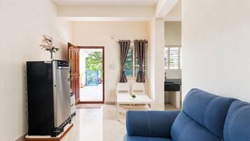 A living room with a sofa, a refrigerator, a dining table with chairs, and a view of the outside.