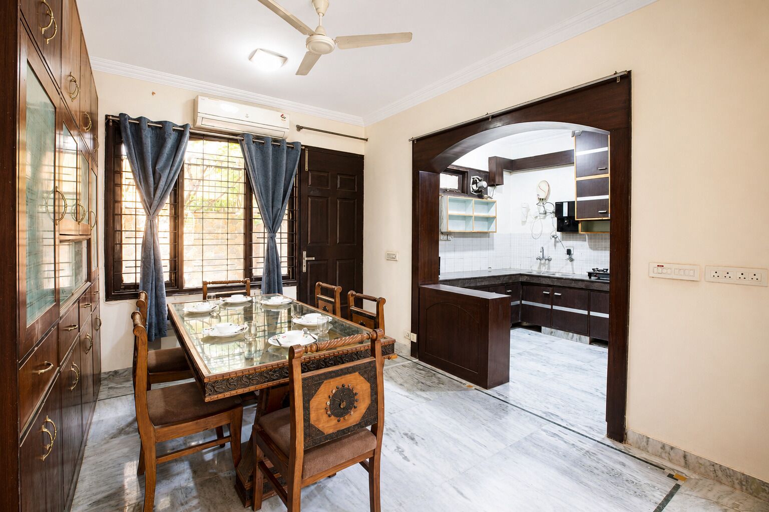 A dining area with a glass-top table, wooden chairs, and a view into the kitchen.