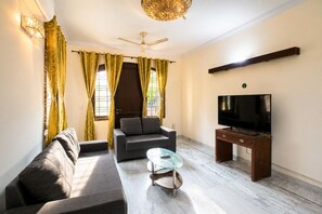 Ein Wohnzimmer mit einer Couch, einem Glastisch, einem Fernseher auf einem Holzgestell und einem Deckenventilator.