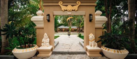 An entrance with a decorative archway, two statues, and a pathway leading to a building.