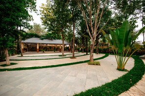 A covered pavilion with a tiled roof, surrounded by a landscaped garden with a paved walkway.