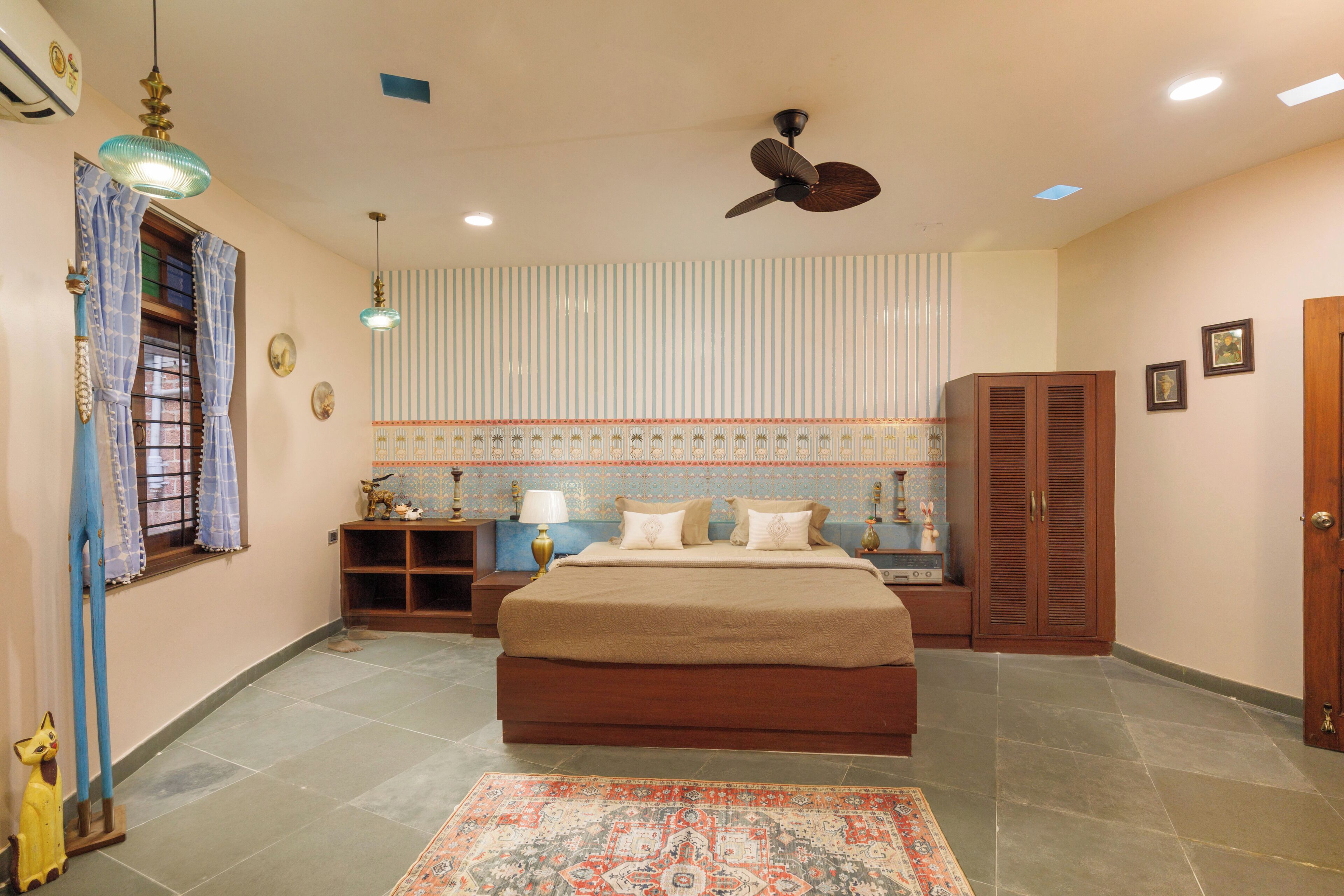 A bedroom with a bed, a ceiling fan, a nightstand, a lamp, a window with curtains, and a door.