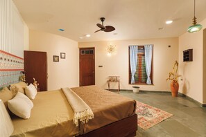 A bedroom with a bed, a ceiling fan, a window with curtains, a small table, and a potted plant.