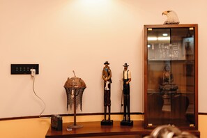 A room with a wooden floor, a wall-mounted electrical outlet, a decorative lamp, and a glass display case containing a Buddha statue.
