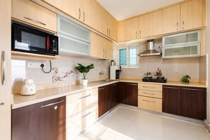 A modern kitchen with wooden cabinets, a microwave, a coffee maker, and a plant. - Pearl Nest by Red Oliveindiranagarnr Manipal (Bengaluru)