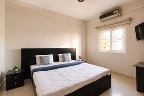 Quarto com cama, mesas de cabeceira, janela e ar condicionado.