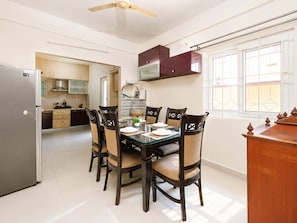 A modern kitchen with a dining area, featuring a refrigerator, cabinets, and a dining table set for four. - Pearl Nest by Red Oliveindiranagarnr Manipal (Bengaluru)