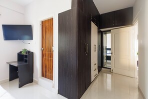 Ein Zimmer mit einem dunklen Holzschrank, einer weißen Tür, einem an der Wand befestigten Fernseher und einer kleinen Pflanze auf einem Regal.