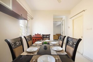 A dining area with a table set for four, surrounded by chairs with woven backs. - Pearl Nest by Red Oliveindiranagarnr Manipal (Bengaluru)