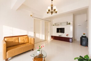 A modern living room with a sofa, a glass coffee table, a TV mounted on the wall, and a ceiling light fixture. - Pearl Nest by Red Oliveindiranagarnr Manipal (Bengaluru)