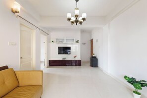 Ein geräumiger Wohnbereich mit Sofa, Flachbildfernseher, einer Kristallleuchter und einer Topfpflanze.
