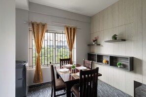 Ein Essbereich mit Tisch für zwei Personen, Stühlen, einem Fenster mit Vorhängen und eingebauten Regalen mit Pflanzen.