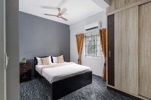Un dormitorio con cama, mesita de noche, armario, ventilador de techo y ventana con cortinas.