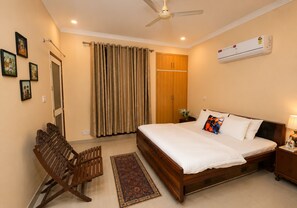 A bedroom with a bed, a wooden chair, a nightstand, a wall-mounted air conditioner, and a ceiling fan.