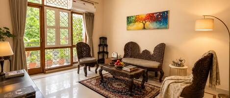 A well-lit living room with a large window, a sofa, a coffee table with books and fruit, and a decorative lamp.