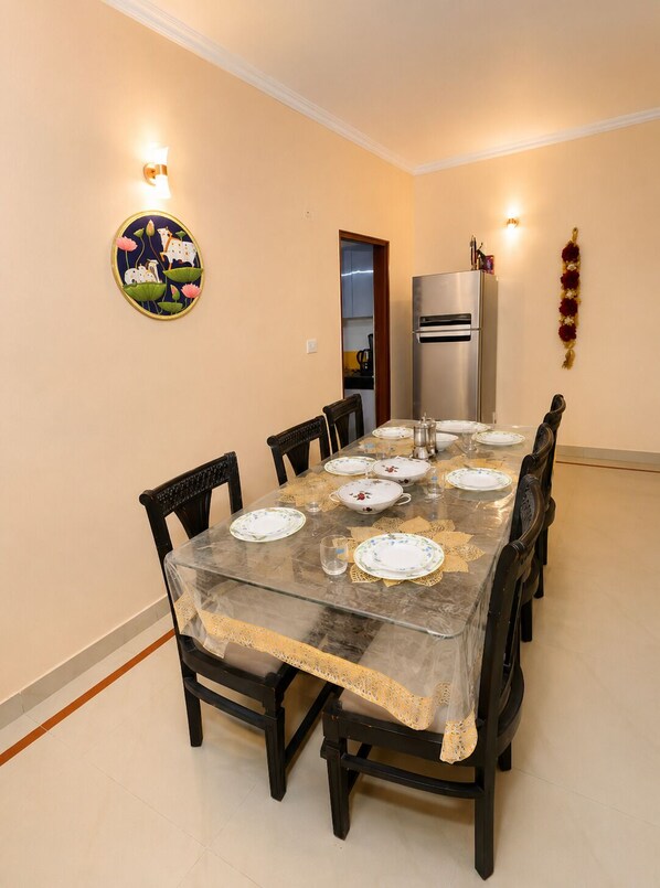 A dining area with a glass table, chairs, and a refrigerator in the background.