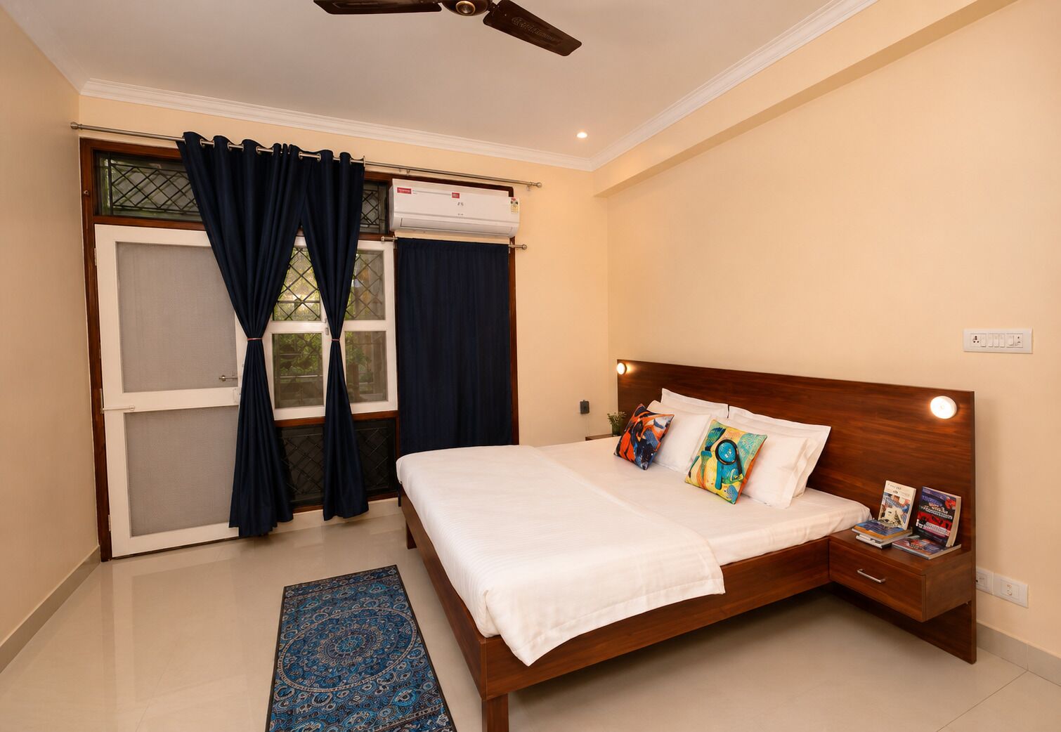 A bedroom with a bed, a nightstand, a window with curtains, a ceiling fan, and a wall-mounted air conditioning unit.