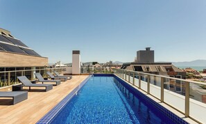 Una piscina en la azotea con sillones de descanso y vistas a la ciudad.