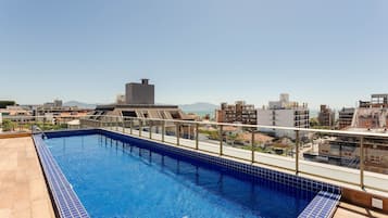 A rooftop swimming pool with a clear view of the cityscape and mountains in the background.