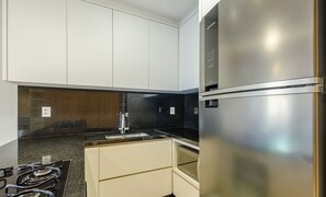 Uma cozinha moderna com eletrodomésticos de aço inoxidável, armários brancos e bancada de granito preto.