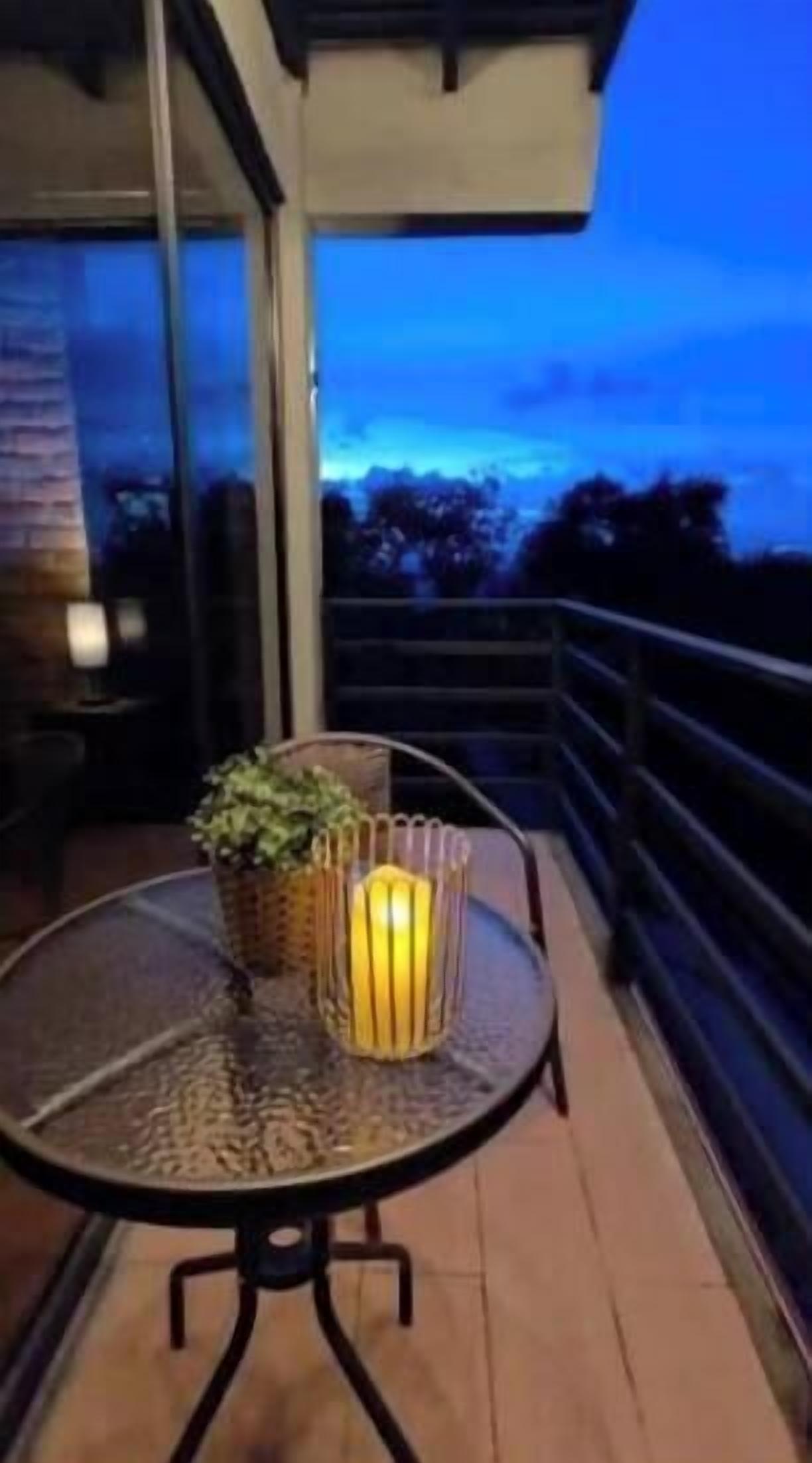 Un balcon avec une table ronde, un pot de fleurs et une bougie.