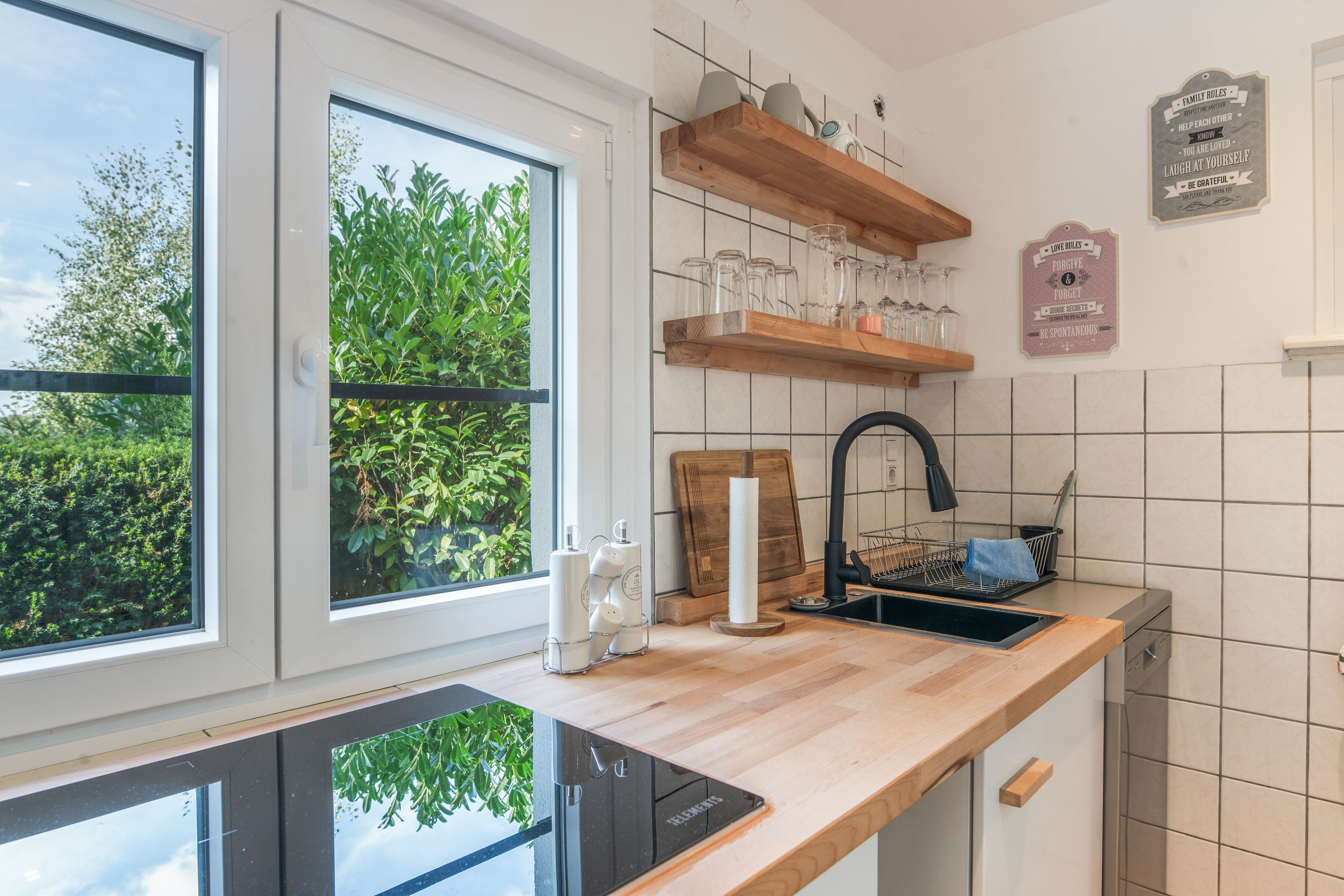 Eine moderne Küche mit einem großen Fenster, Holzregalen und einem schwarzen Wasserhahn.