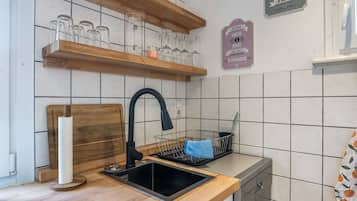 Cuina amb un rentaplat de color negre, taulell de fusta i una prestatgeria penjant amb vetrereria.