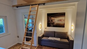 Et værelse med trægulv, en grå sofa, en træstige og et billede hængende på væggen.