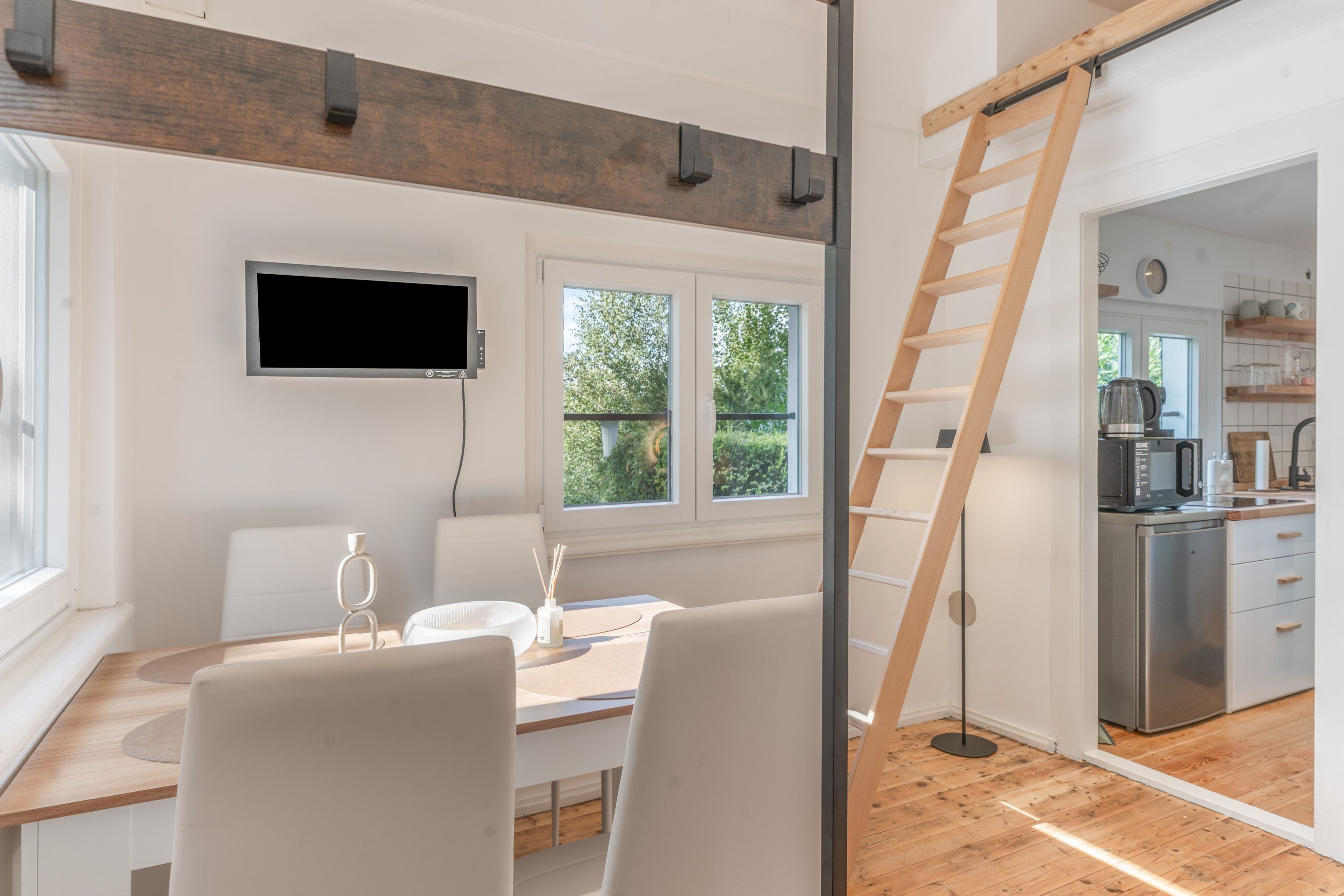 A modern kitchen with a built-in microwave, a wooden ladder, and a view of the outdoors through large windows.