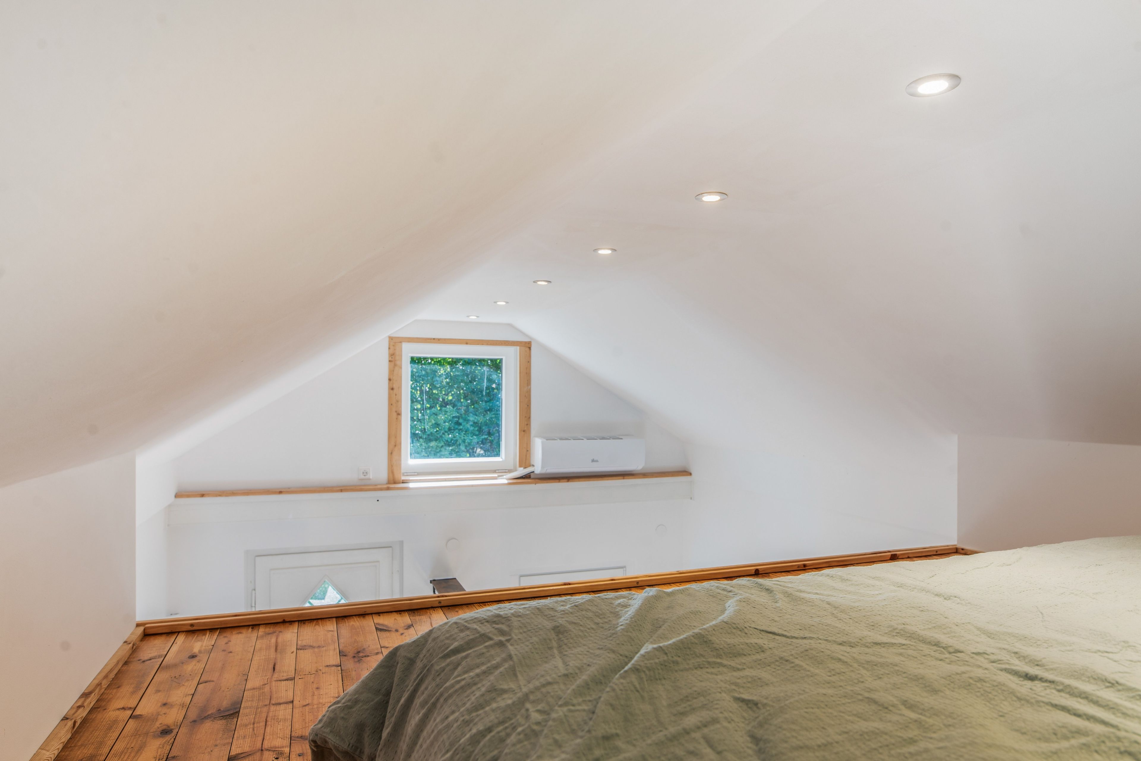 Quarto com teto inclinado, janela com vista para vegetação e aquecedor embutido.