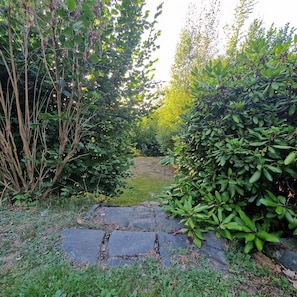 A stone pathway leading through a garden with dense foliage on either side. - Vacation Home 'Haus Labaily Lake & Sauna' with Lake View, Wi-Fi, and Air Conditioning (Mittweida)